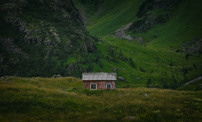 青山边草地上的棕色和白色小屋